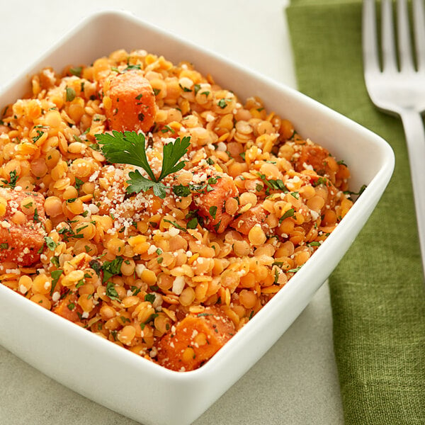 A close-up of a bowl of red lentils with spices and parsley.