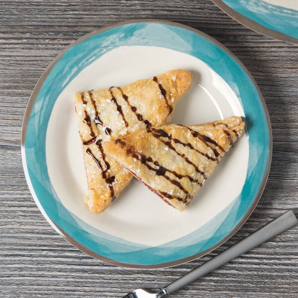 A Kanello ivory melamine plate with blue diamond edge holding two pastries with chocolate syrup.