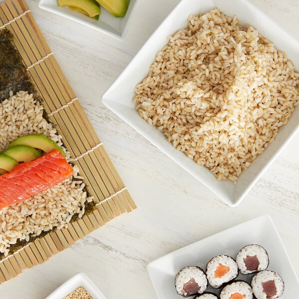 A wooden table with white bowls of sushi rice and vegetables and a plate of Regal brown rice and sushi.