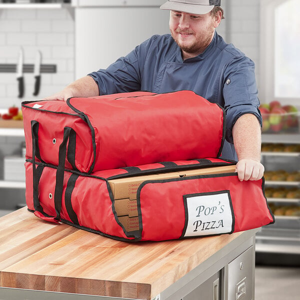 A man holding a red CaterGator Dash insulated pizza delivery bag with pizza boxes inside.