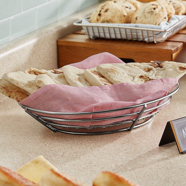 Stainless steel oval basket with bread on a counter.