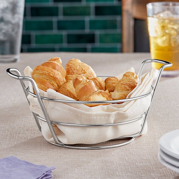 A Clipper Mill stainless steel basket filled with croissants sits on a table.