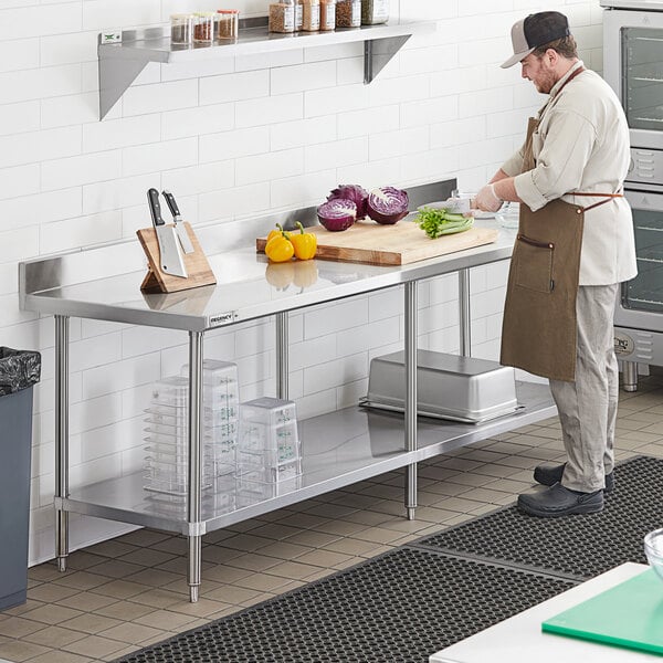 A man in a brown apron standing at a Regency stainless steel work table with undershelf in a kitchen.
