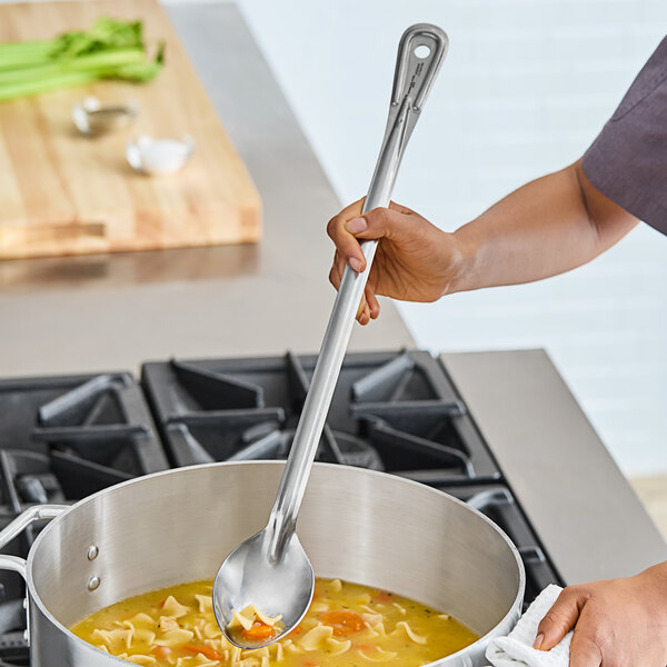 A person using a Vollrath stainless steel basting spoon to stir soup in a pot.
