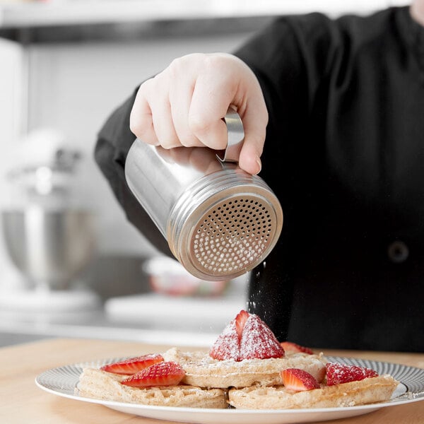 A person using a Vollrath stainless steel shaker to pour powder on food.