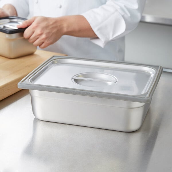 A chef using a gray Vollrath silicone band to prepare food in a stainless steel pan.