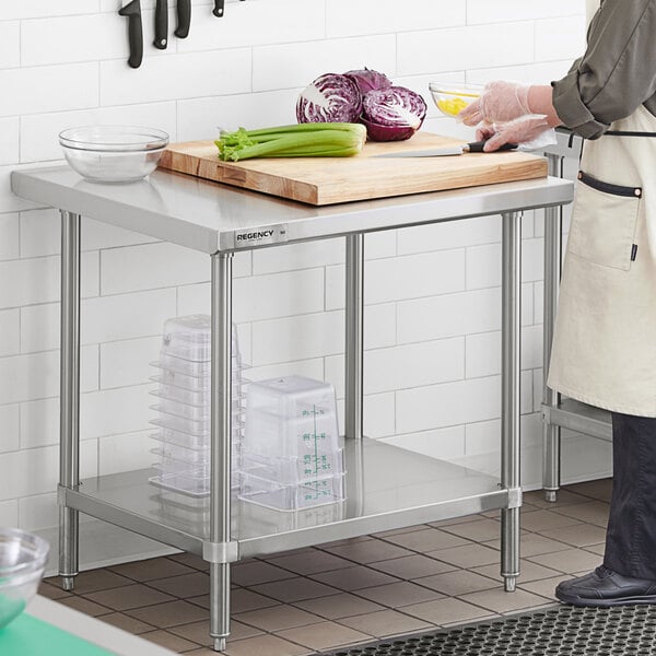 A woman in a white apron using a Regency stainless steel work table with undershelf to prepare food.