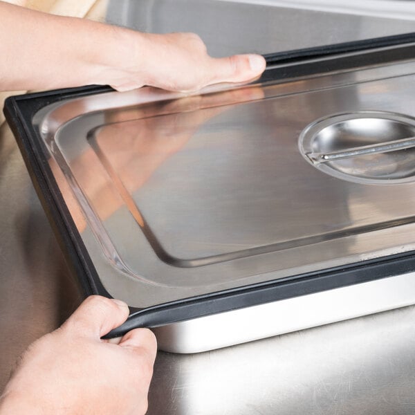 A person holding a black Vollrath silicone band on a metal tray.