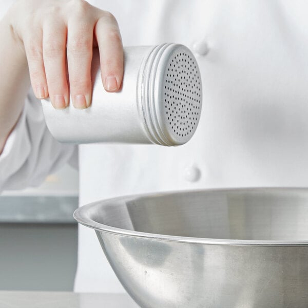 A chef using a Vollrath aluminum shaker to pour salt into a bowl.