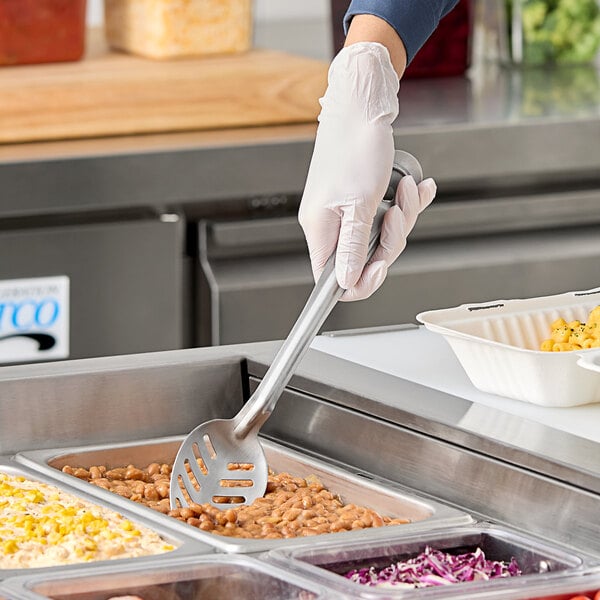 A person in white gloves using a Vollrath slotted basting spoon to serve food.