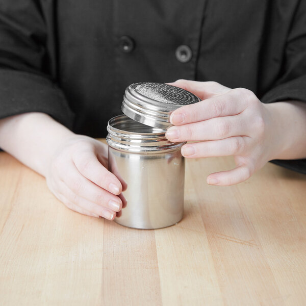 A person holding a Vollrath stainless steel shaker/dredge.