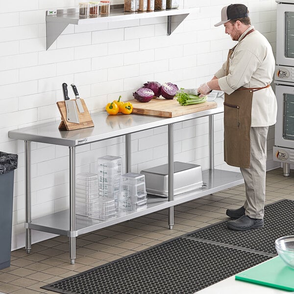 A man in a chef's outfit cutting vegetables on a Regency stainless steel work table with undershelf.