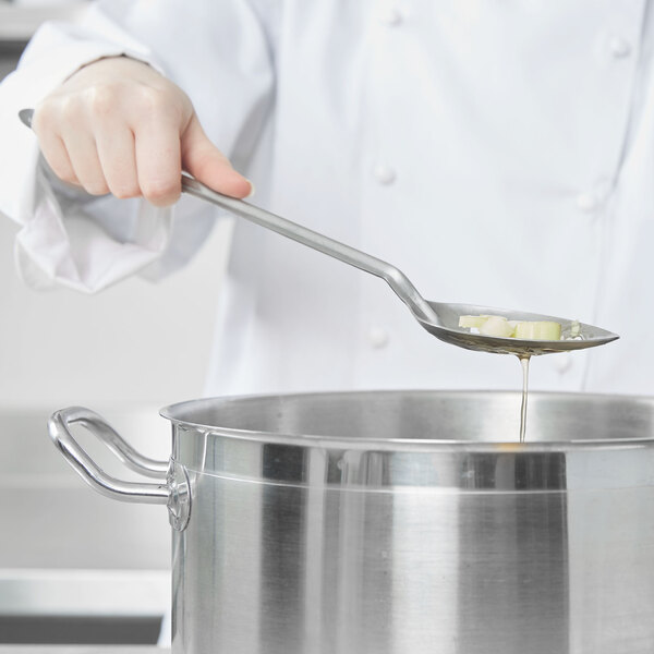 A person using a Vollrath slotted stainless steel basting spoon to stir food in a pot.