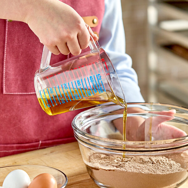 A person pouring oil into a bowl using a Rubbermaid clear polycarbonate measuring cup.
