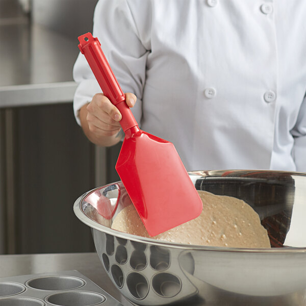 A person using a Carlisle red paddle to mix dough in a bowl.