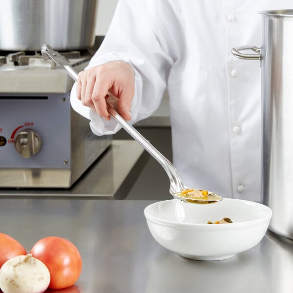 A chef using a Vollrath hooked handle solid spoon to prepare food in a bowl.