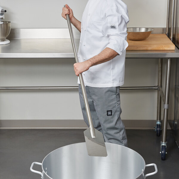 A man using a Carlisle stainless steel paddle to stir a large pot.