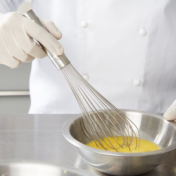 A person in white gloves using a Vollrath stainless steel whisk to mix eggs in a bowl.