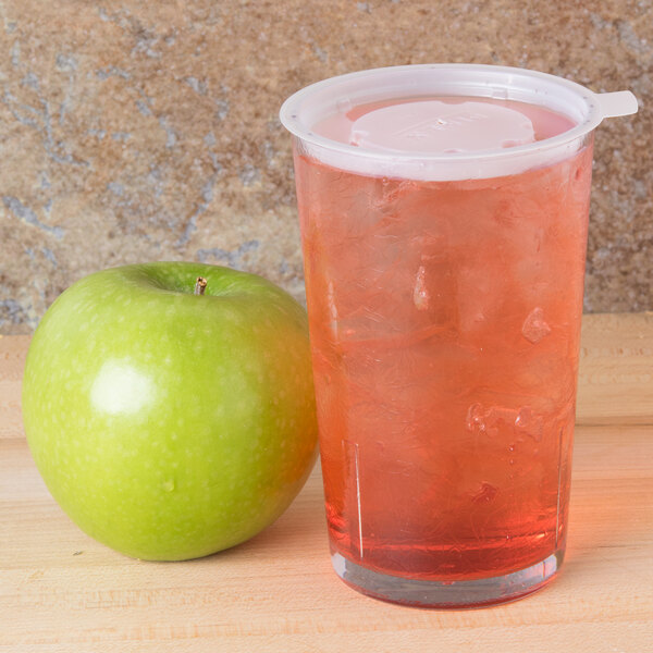 A Cambro plastic tumbler filled with a pink drink on a white background next to a green apple.