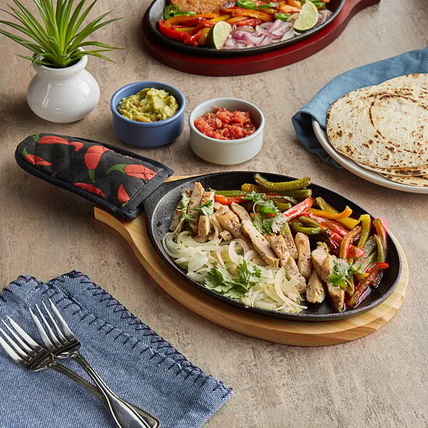 A Choice oval cast iron fajita skillet with chicken, vegetables and tortillas on a table.