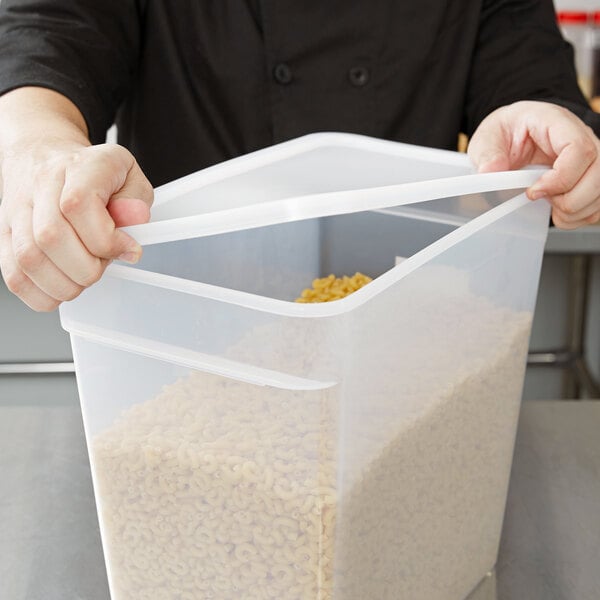 A person opening a Carlisle translucent rectangular plastic food storage container filled with pasta.