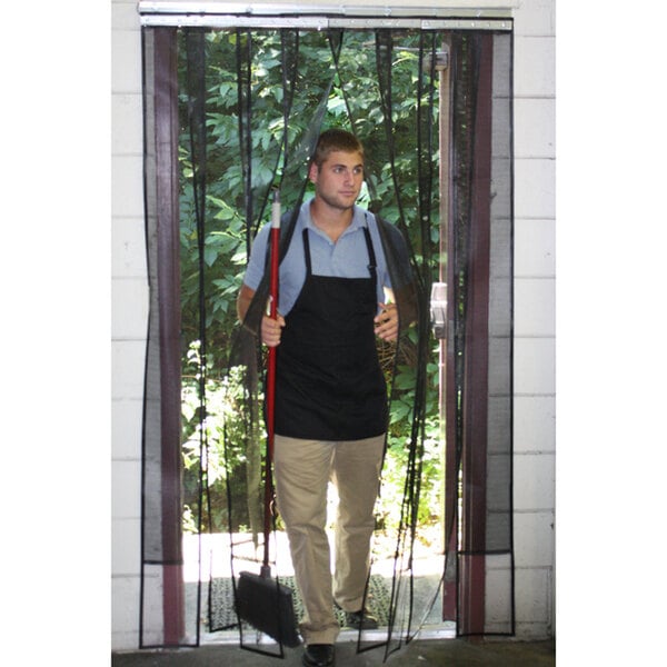 A man wearing a black apron holding a broom and a net standing in front of a black rectangular mesh curtain.