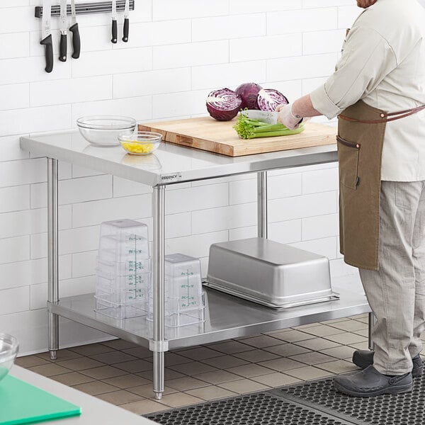 A man in a chef's uniform cutting vegetables on a Regency stainless steel work table with undershelf.