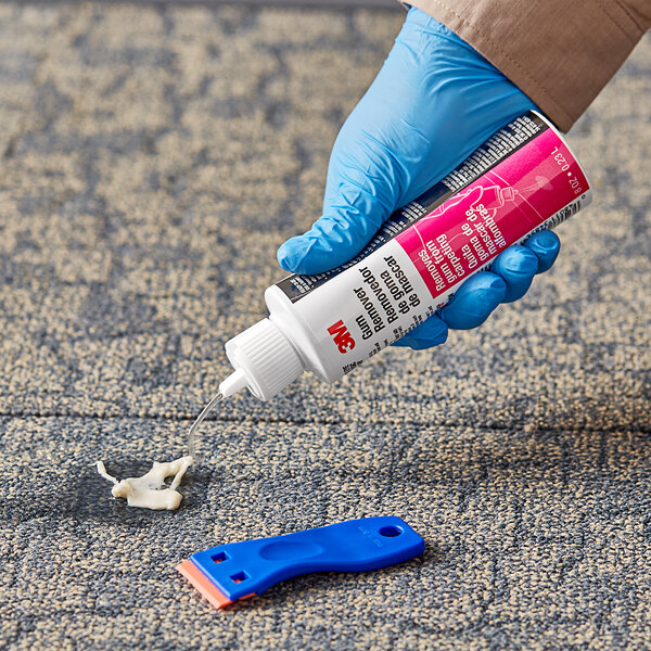 A hand in a blue glove using 3M Gum Remover on a blue plastic surface.