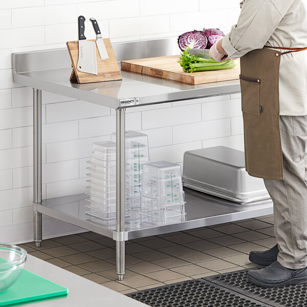 A man in a chef's uniform cutting vegetables on a Regency stainless steel work table with undershelf.