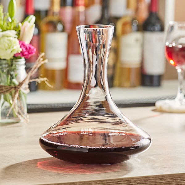 An Acopa glass wine decanter filled with red wine on a table.