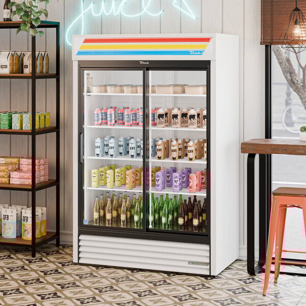 A white refrigerated sliding glass door merchandiser with LED lighting, stocked with various beverages.