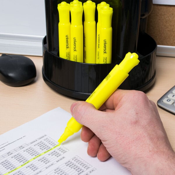 A hand holding a Universal fluorescent yellow chisel tip highlighter over a piece of paper.