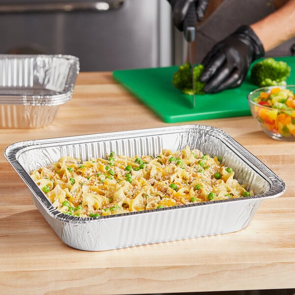 A person cutting vegetables in a Choice foil steam table pan on a table.