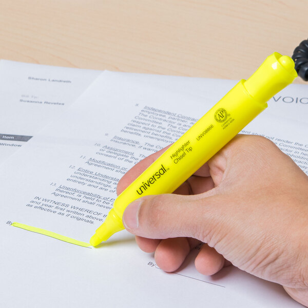 A hand holding a Universal fluorescent yellow highlighter pen over a paper.