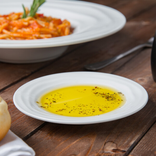 A Tuxton TuxTrendz bright white china sauce dish filled with olive oil on a table.