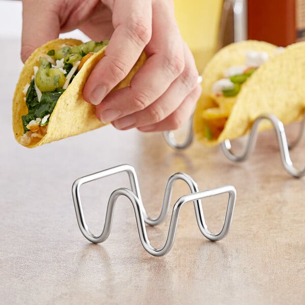 A person holding tacos over a stainless steel wire taco holder.