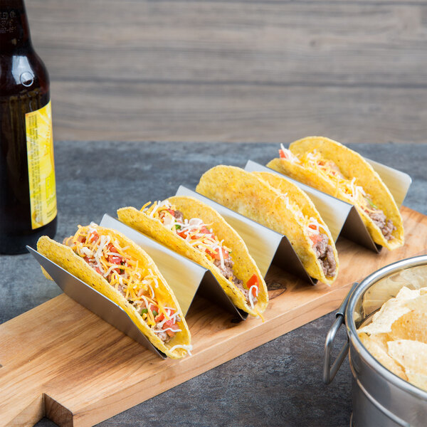 four tacos in a taco holder beside a beer bottle