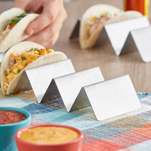 A person holding a taco on a stainless steel taco holder.