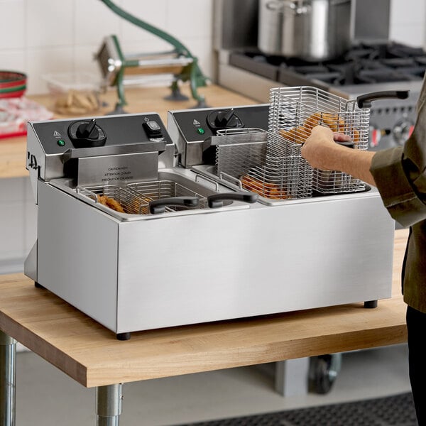 A stainless steel dual-basket commercial countertop deep fryer on a wooden table.