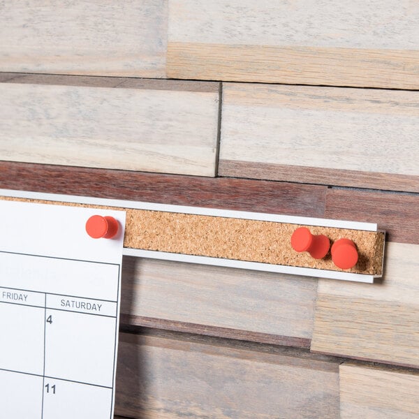 A hand hanging a calendar on a Universal brown cork bulletin bar.