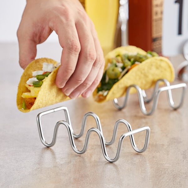 A hand holding a taco over a stainless steel wire taco holder.