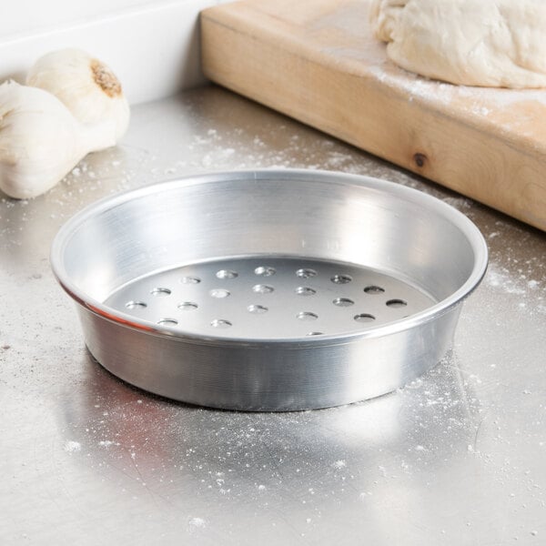 An American Metalcraft silver aluminum pizza pan with holes in it filled with dough.