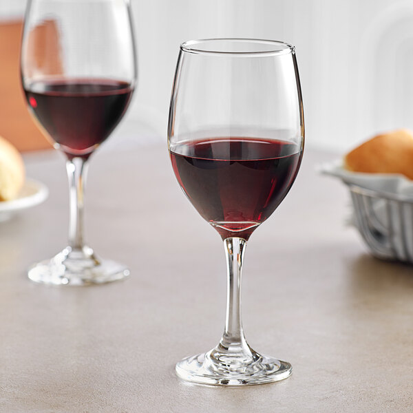 Two Acopa all-purpose wine glasses on a table with a glass of red wine.