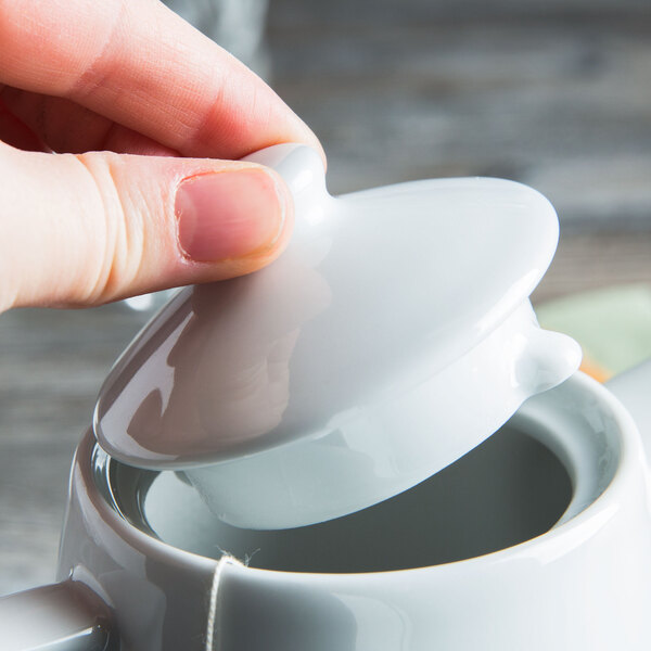 A person opening a Tuxton Bright White China teapot lid.