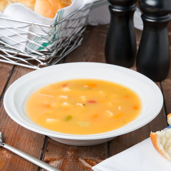 A Tuxton TuxTrendz bright white china soup bowl on a table with bread and salt and pepper.
