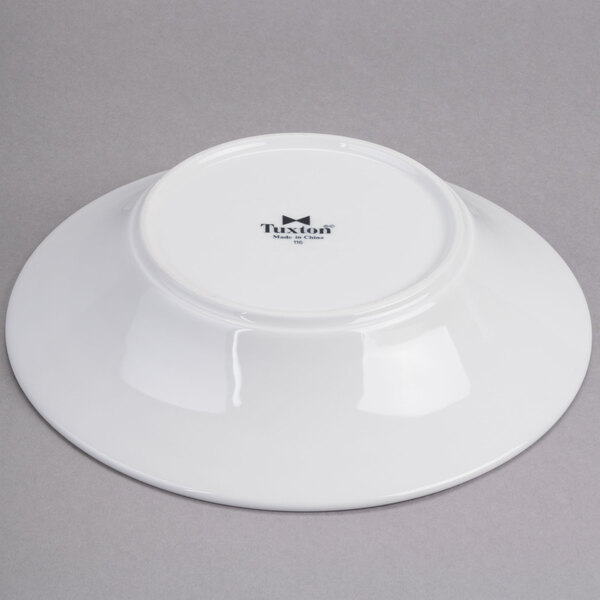 A white Tuxton china soup bowl with a white rim and black text on it.