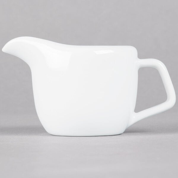 A white Tuxton creamer with a handle.