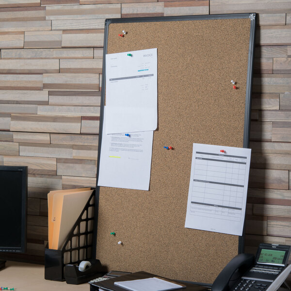 A Universal cork board with black frame with papers pinned to it.