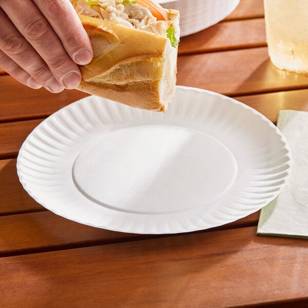 A plain white 9-inch uncoated paper plate on a wooden table.