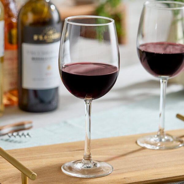 A clear 16 oz. wine glass partially filled with red wine, placed on a wooden surface.